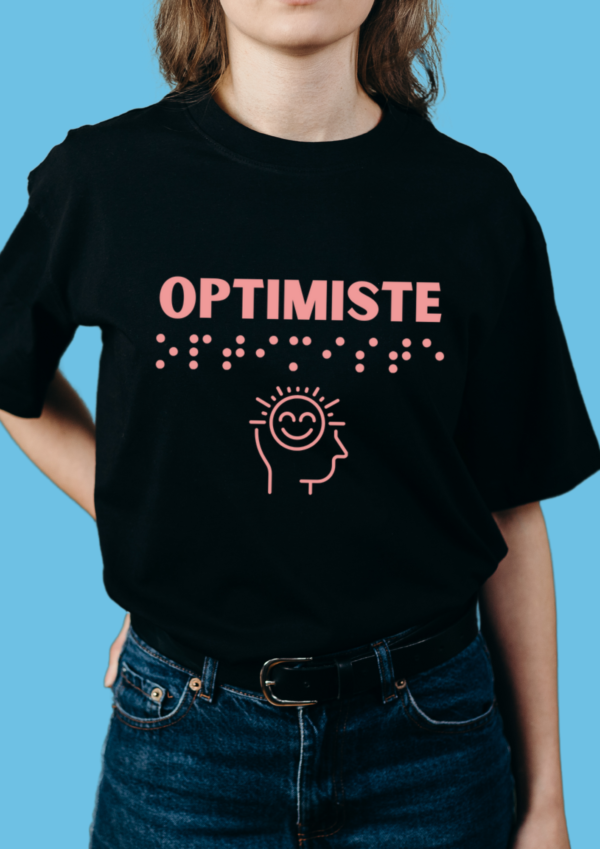 une femme portant un t shirt avec pour inscription optimiste en relief en braille rose. T-shirt inclusif, design accessible, mode tactile pour non-voyants et malvoyants.